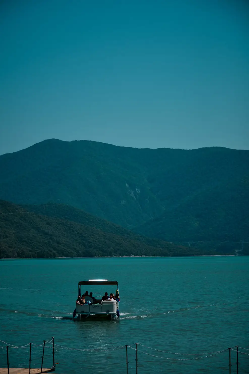 Small boat carrying passengers across a calm lake with forested mountains in the background.