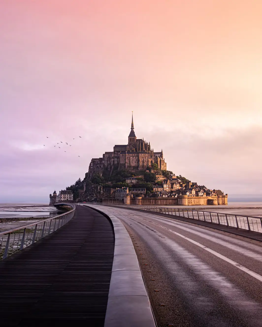 Mont Saint-Michel abbey silhouetted at sunset with the causeway leading toward it