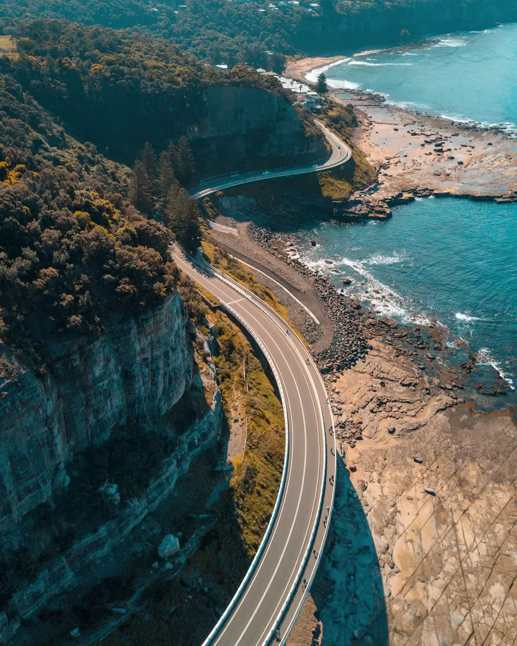 Aerial view of Sea Cliff Bridge winding along a coastal cliff with the ocean and rocky shoreline in New South Wales, Australia
