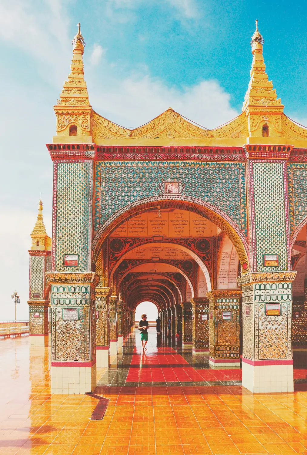 Colourful tiled arched corridor of Myanmar Buddhist temple with repeating archways and lone visitor, Myanmar
