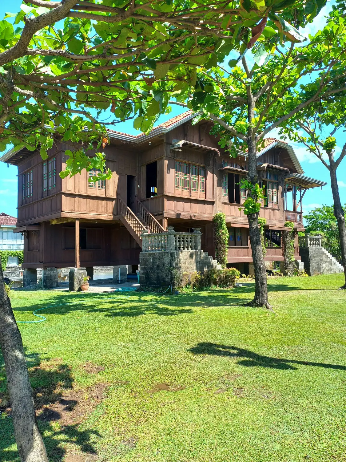Traditional wooden ancestral house surrounded by green lawn and trees in the Philippines.