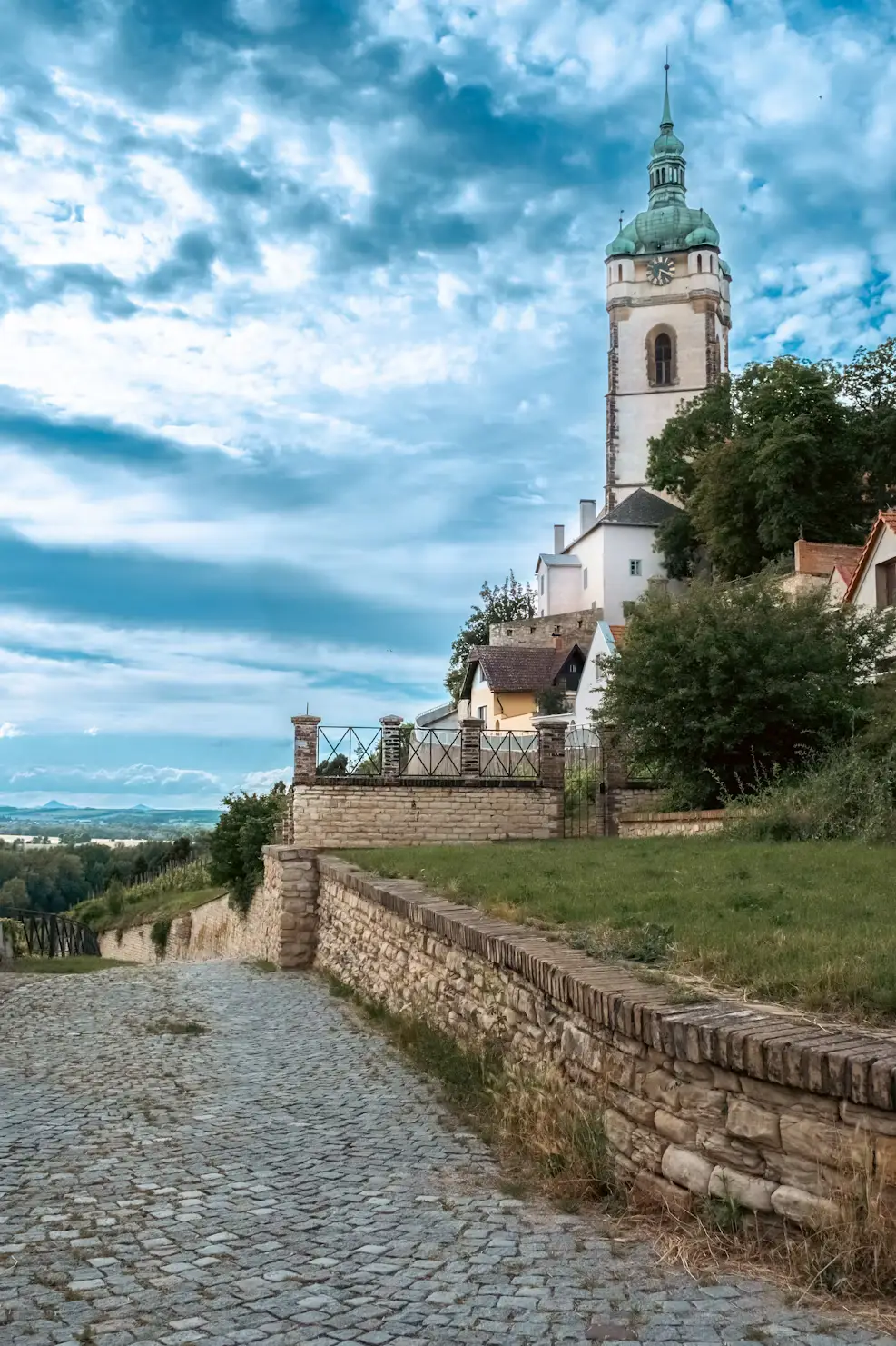 Cobblestone pathway leading to a church tower on Petřín Hill under a partly cloudy sky