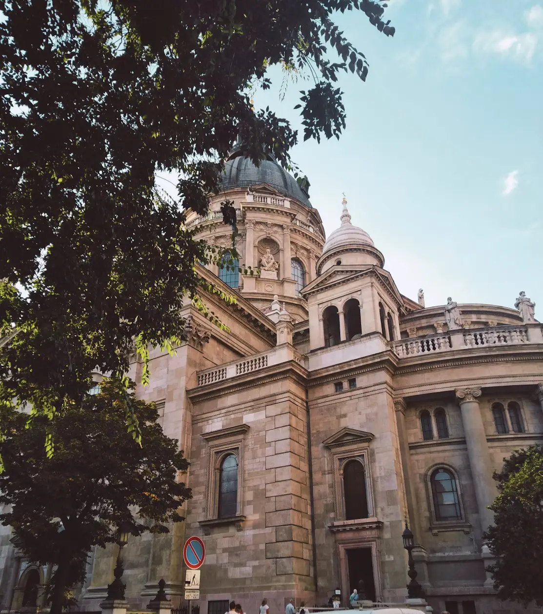 Historic domed basilica partially framed by leafy trees under a clear sky.