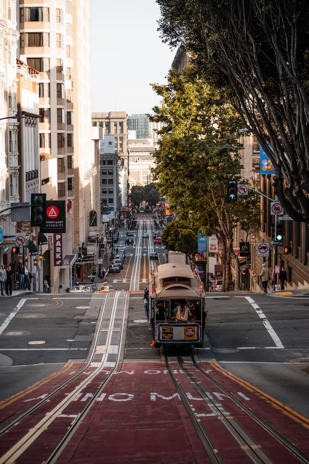 A cable car travelling down a tree-lined San Francisco street between tall buildings.