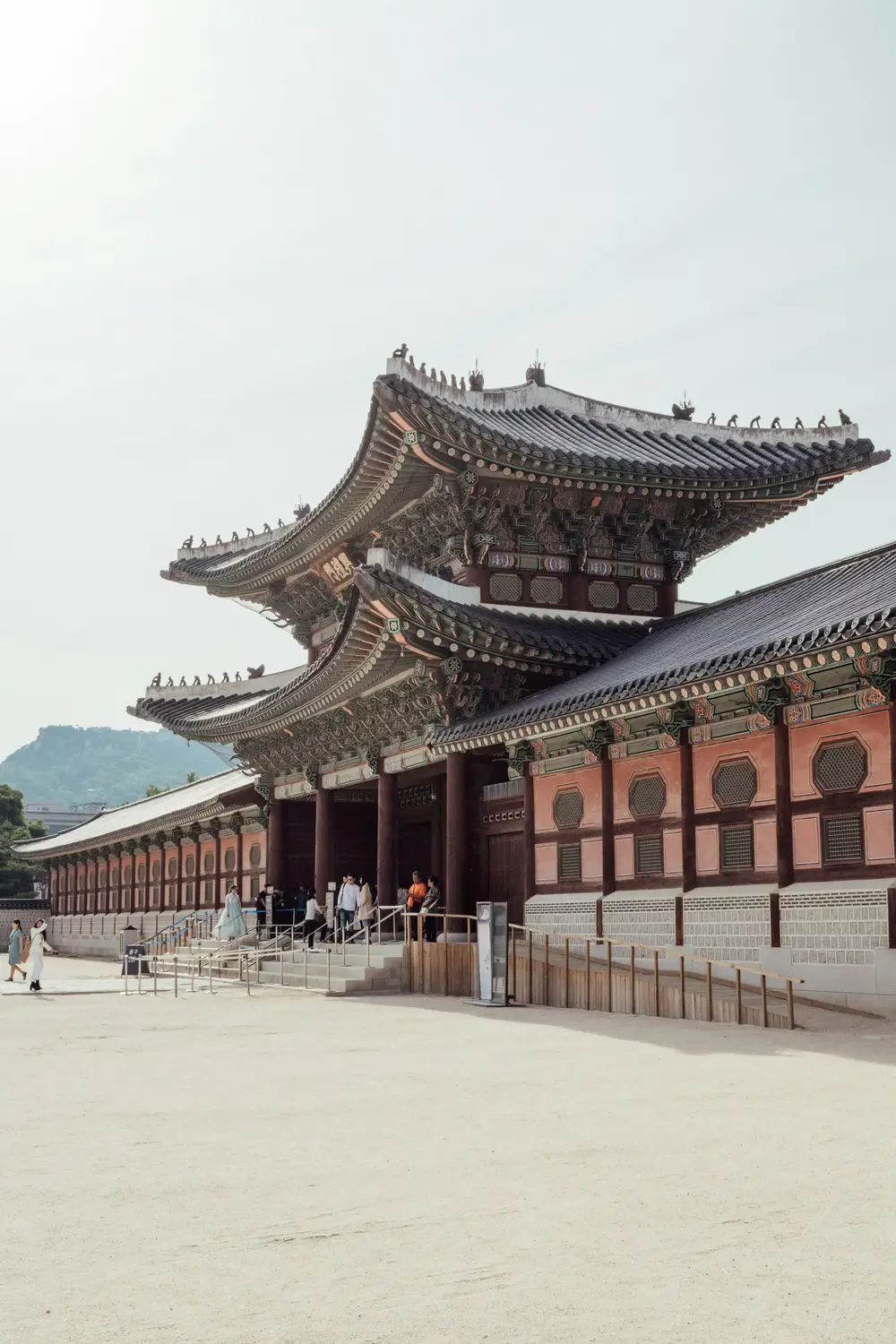 Two-tiered gate of Gyeongbokgung Palace with curved tiled roofs and traditional Korean architecture, with visitors entering on a sunny day in Seoul.