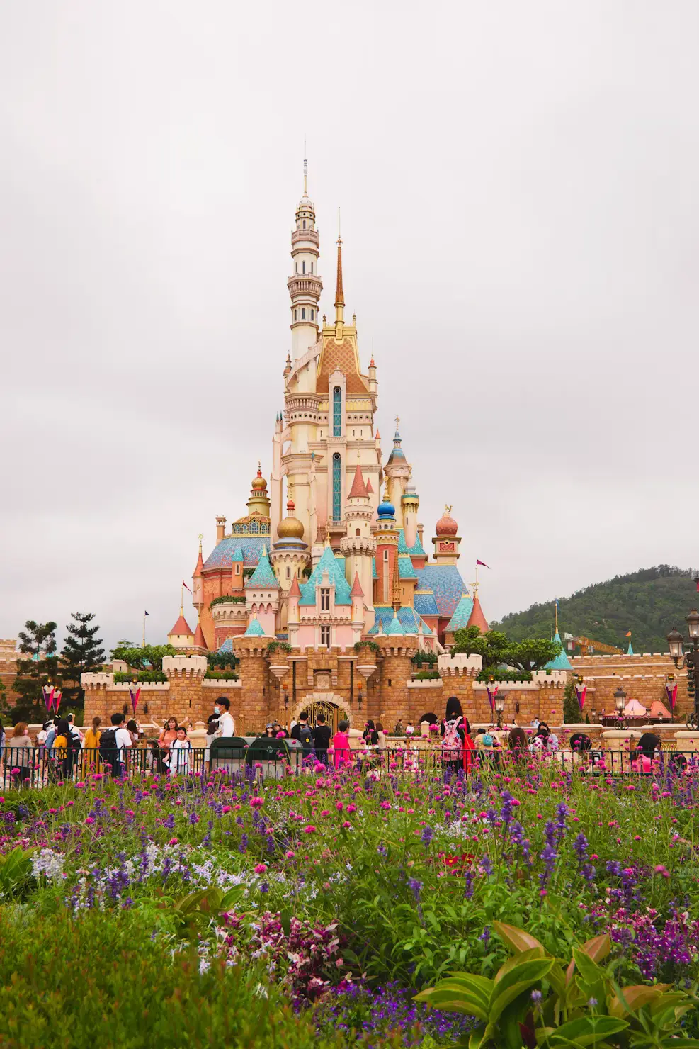 Disneyland castle surrounded by colorful flower gardens under a cloudy sky in Hong Kong.