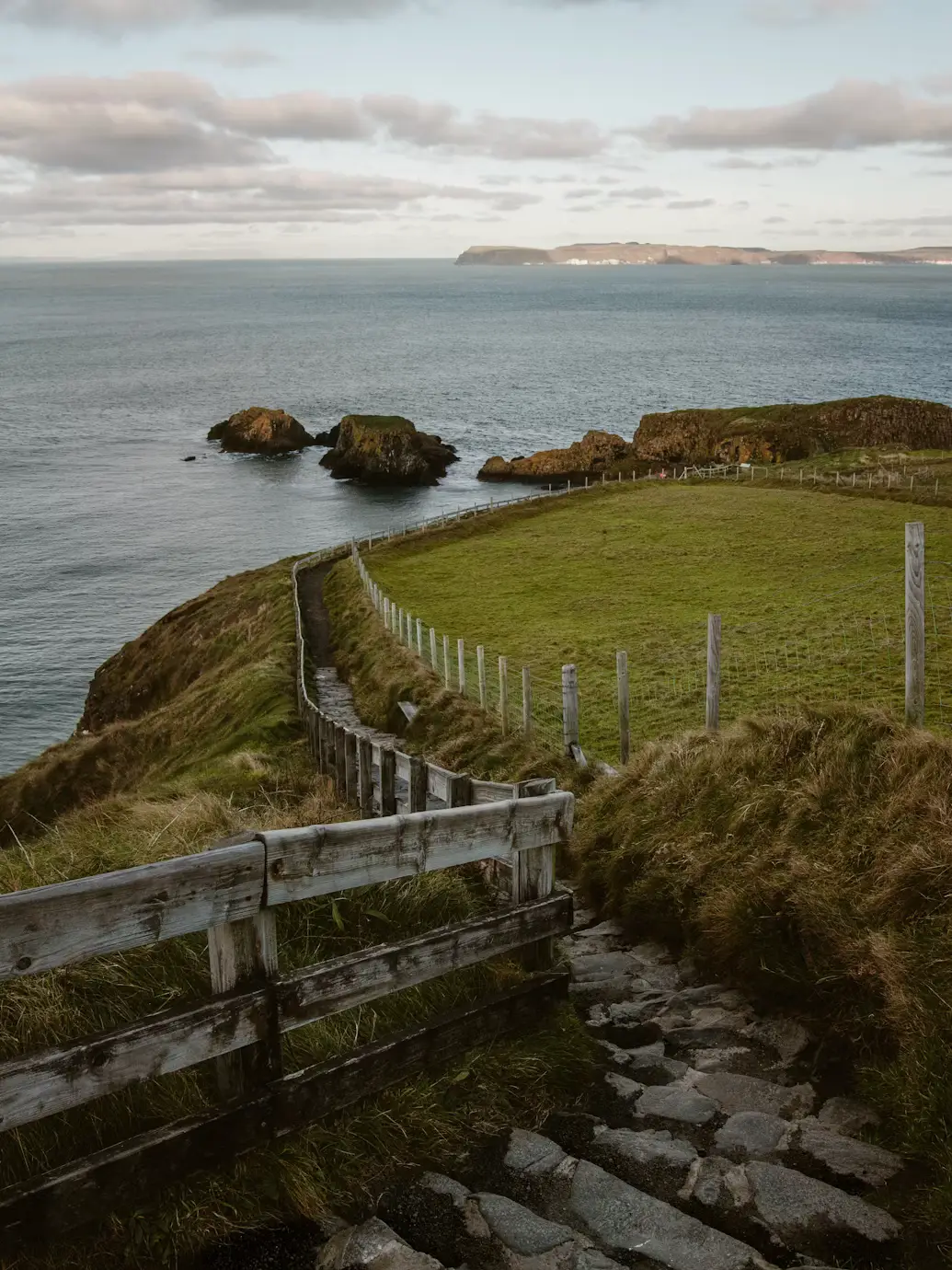 Coastal cliffside path with a wooden fence overlooking rocky sea stacks, Ireland