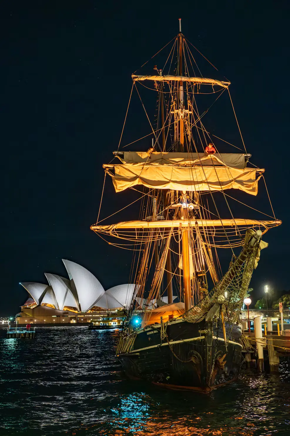 Tall ship illuminated at night with the Sydney Opera House in the background