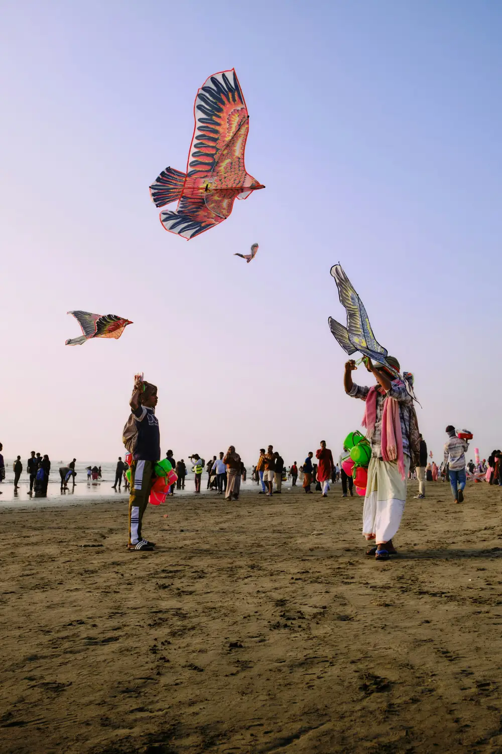 Kite sellers flying colorful eagle-shaped kites on Cox's Bazar beach with crowd of tourists in background, Bangladesh