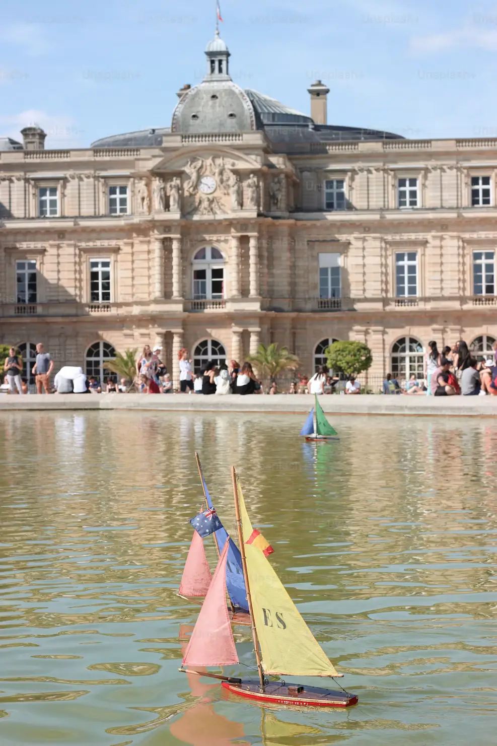 Toy sailboats floating on the pond at Jardin du Luxembourg with the palace behind