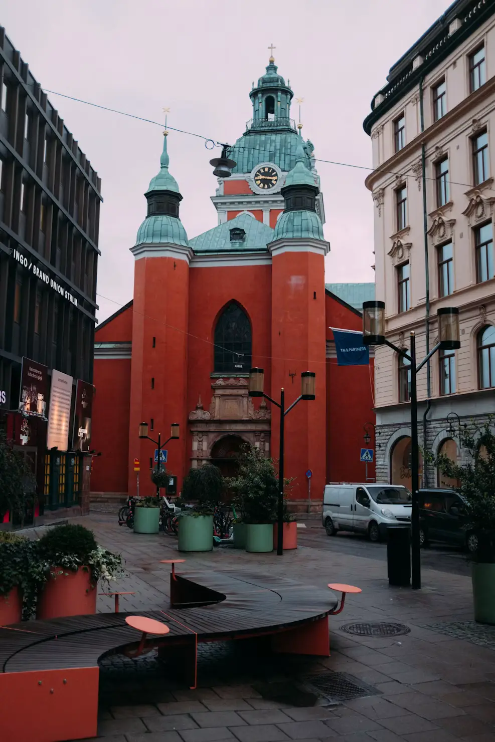Red brick church tower with a green dome, seen from a small plaza with outdoor seating.