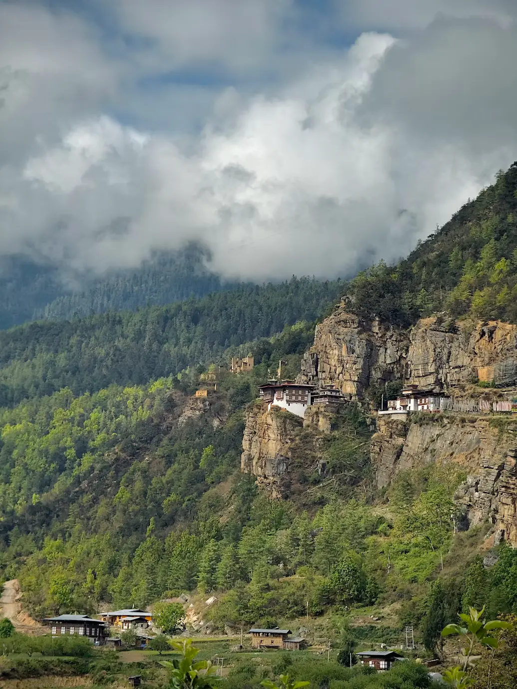 Rugged forested mountain cliffside shrouded in clouds over a river valley in Bhutan.
