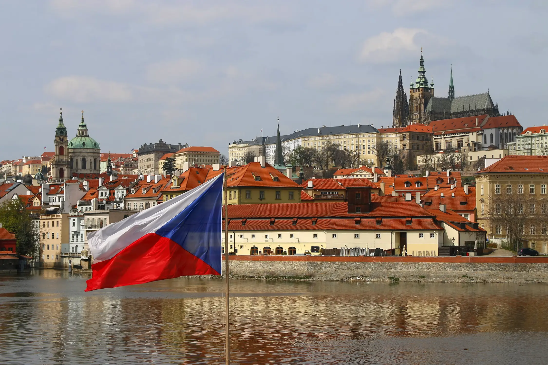 Czech national flag flying over the Vltava River with Prague Castle and St. Vitus Cathedral in the background