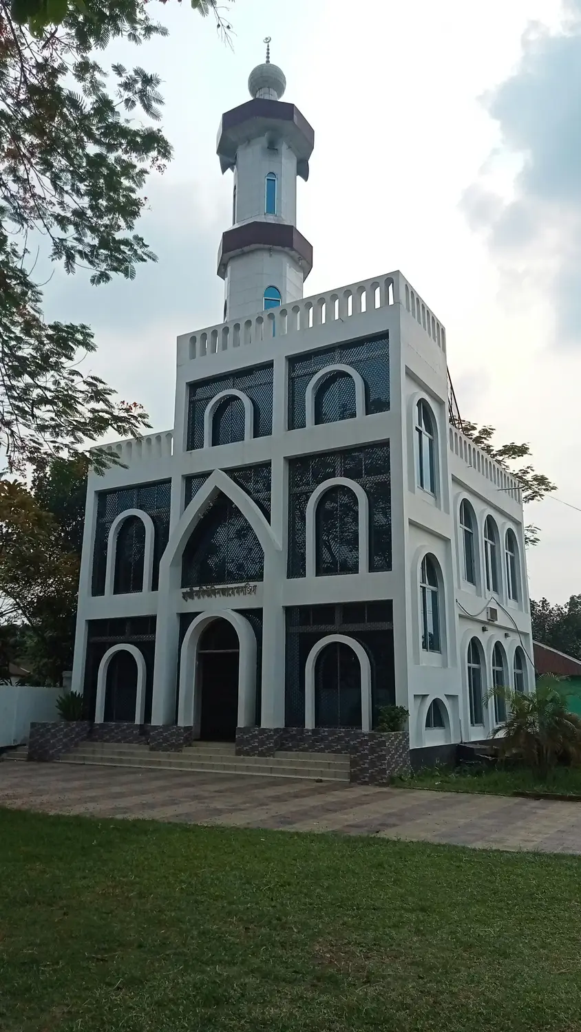 White two-storey mosque with single minaret and arched windows surrounded by green trees, Bangladesh