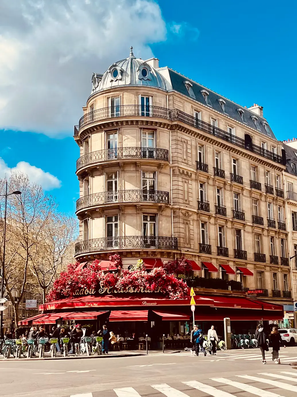 Corner café with red awnings beneath a classic Haussmann-style building in Paris
