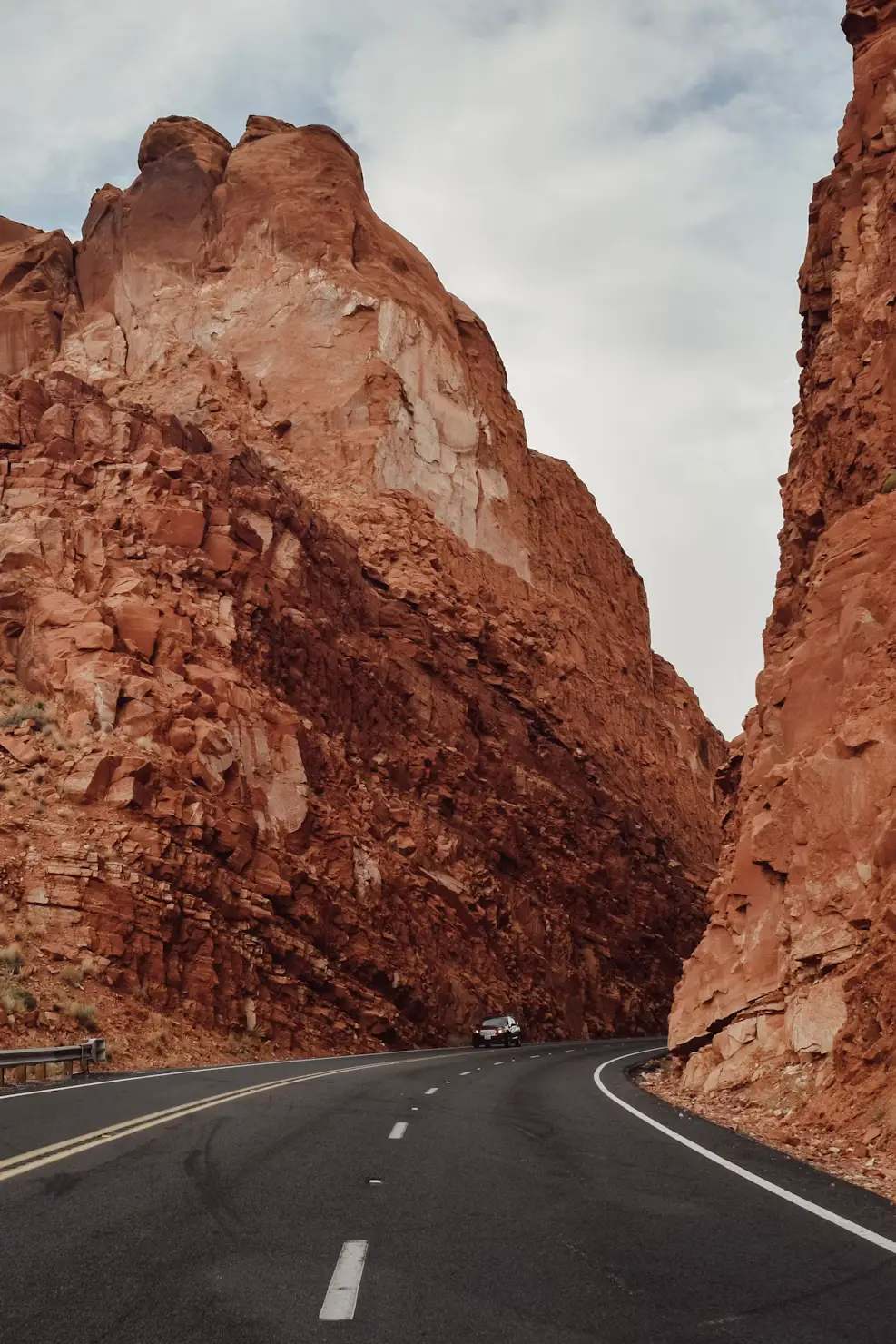 A highway curving through a narrow canyon of towering red rock cliffs. Shorter option: