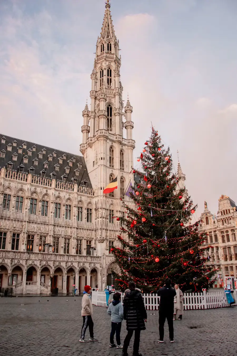 A decorated Christmas tree in front of Brussels' Town Hall in the Grand Place, with a family looking on.