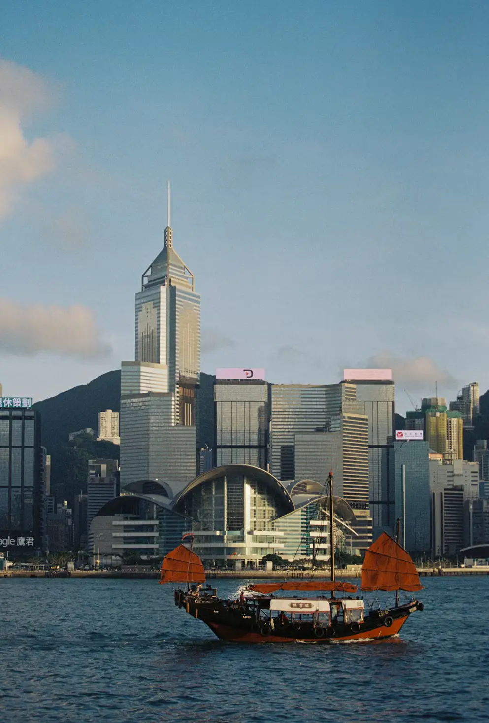 Traditional red-sailed Chinese junk boat sailing across Victoria Harbour with the city skyline in the background in Hong Kong.