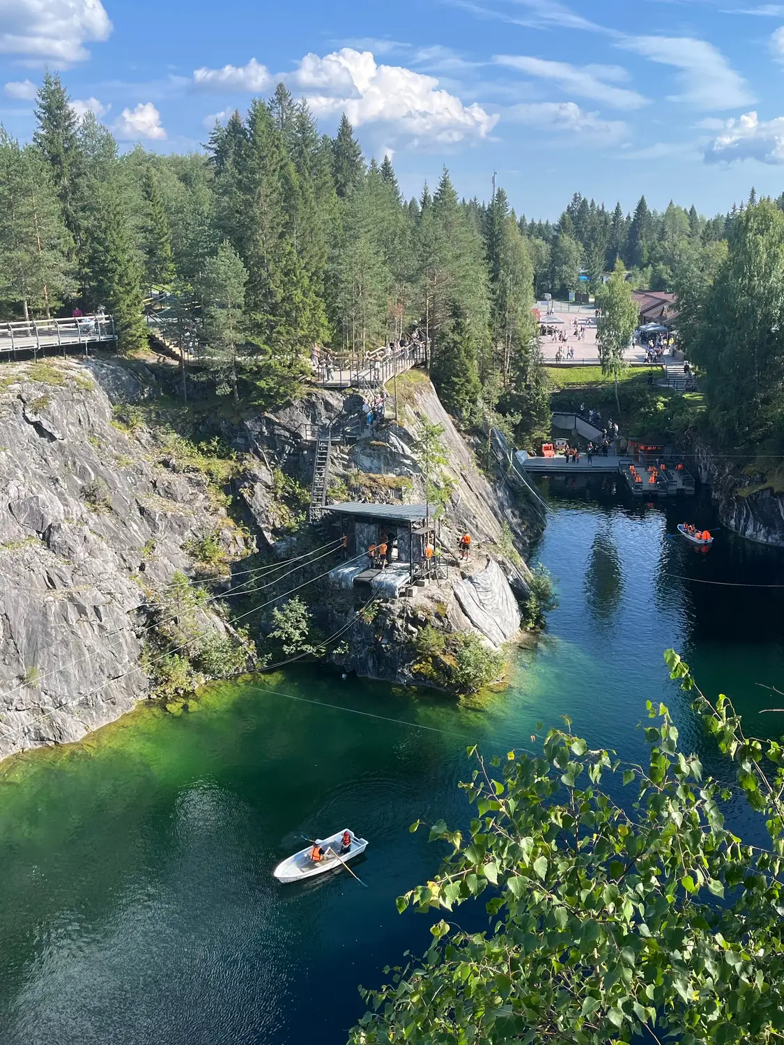 A scenic rocky gorge with clear green-blue water, forested cliffs, walking paths, and small boats.