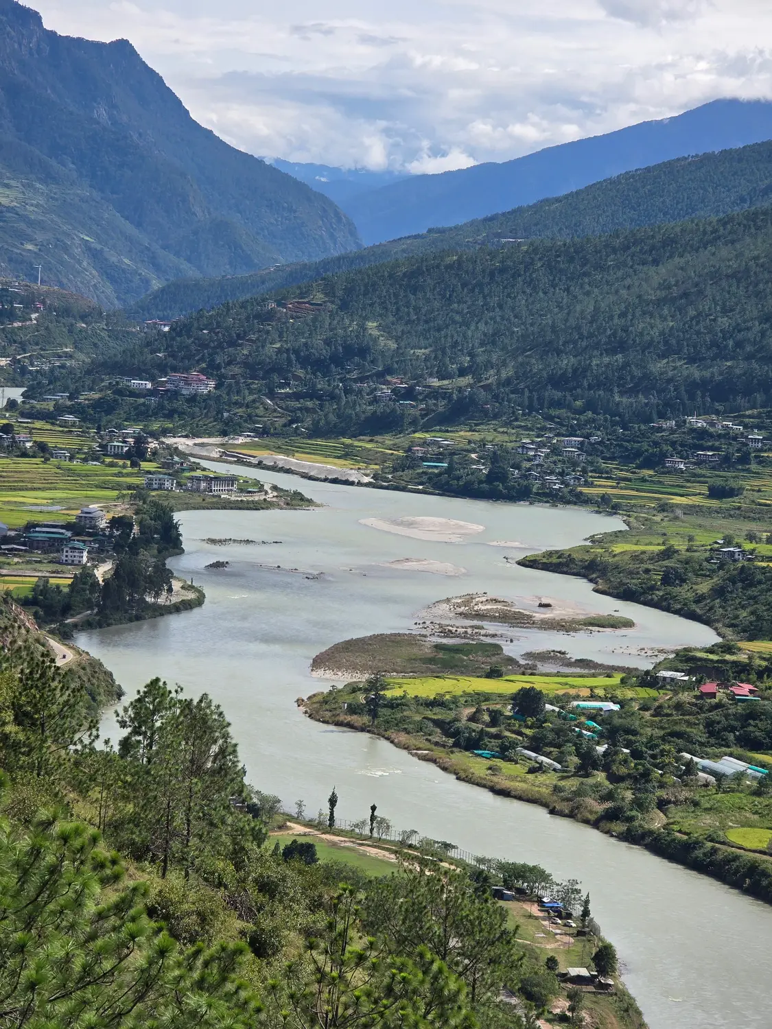 Scenic view of a winding river cutting through a green Himalayan valley with terraced fields in Bhutan.