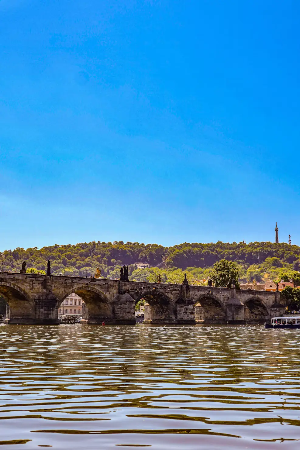 Wide view of Charles Bridge's stone arches spanning the Vltava River under a clear blue sky