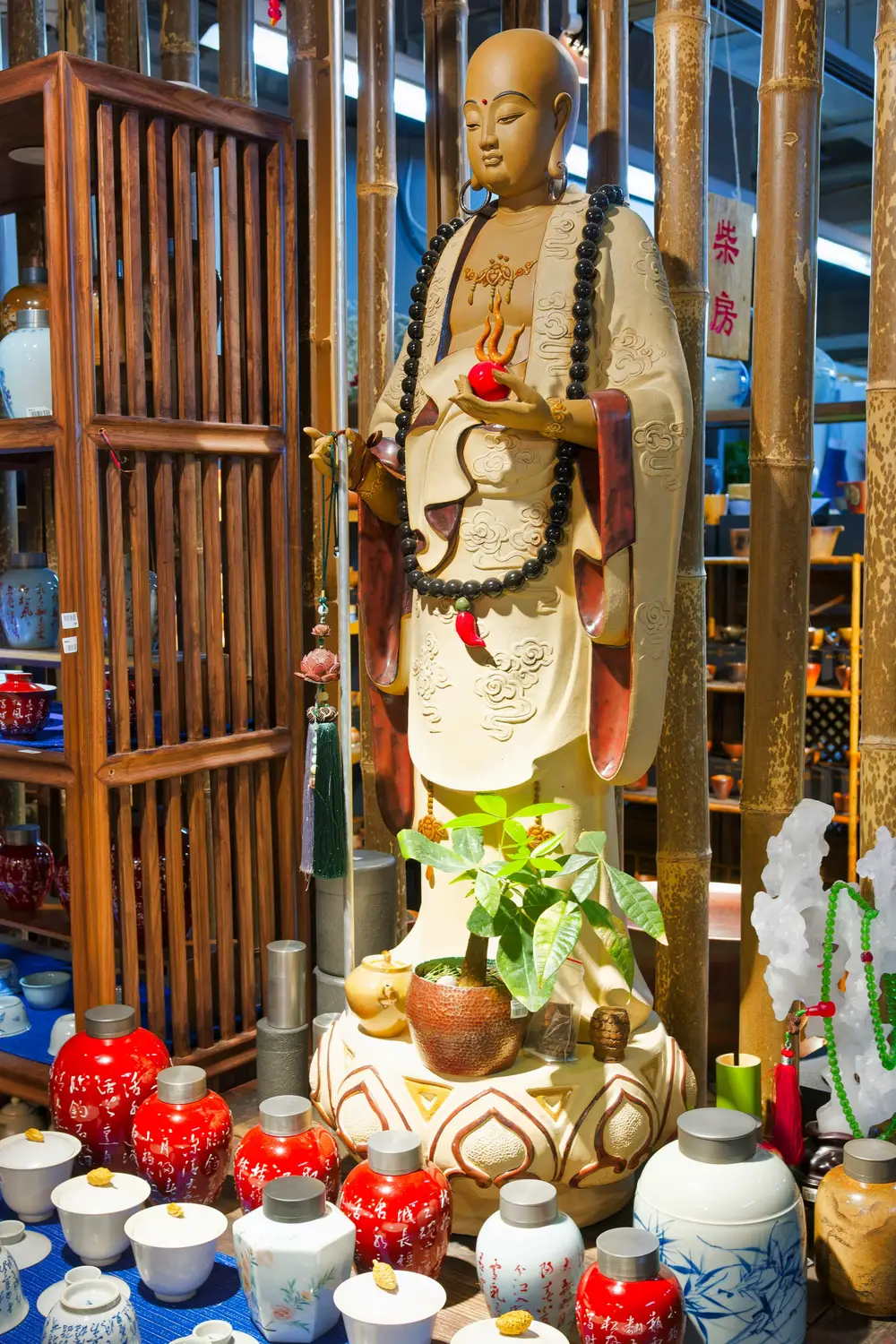 Buddhist monk statue holding peach in Chinese tea market surrounded by ceramic teaware and bamboo decor