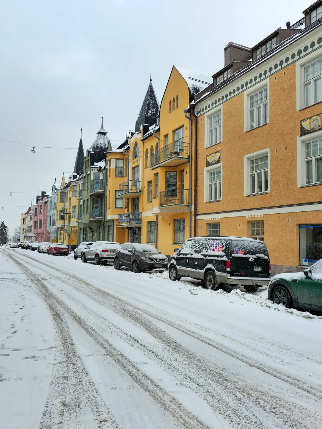 Snow-covered city street lined with colorful historic buildings and parked cars.
