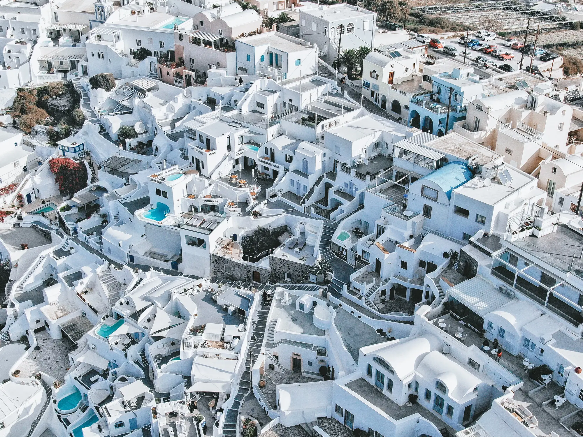 Aerial view of a hillside village with whitewashed buildings, winding stairways, and small turquoise pools.