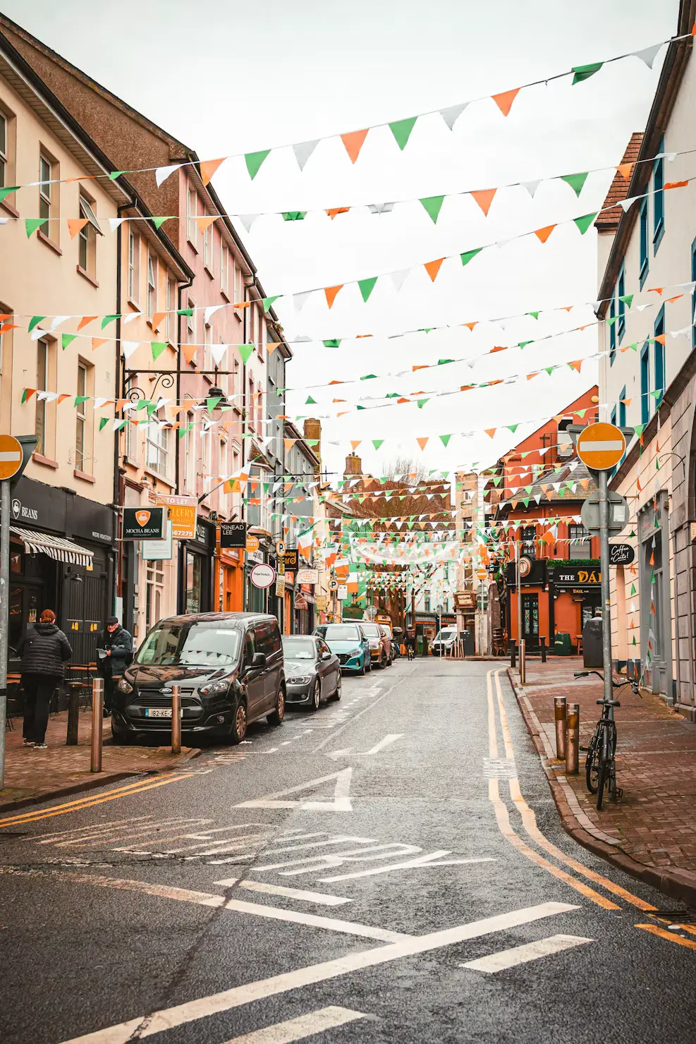 Colorful shopfronts along a cobblestone street decorated with triangular flag bunting, Ireland.