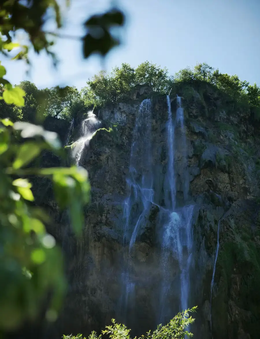 Multiple thin waterfalls cascading down a moss-covered rock face surrounded by green trees.