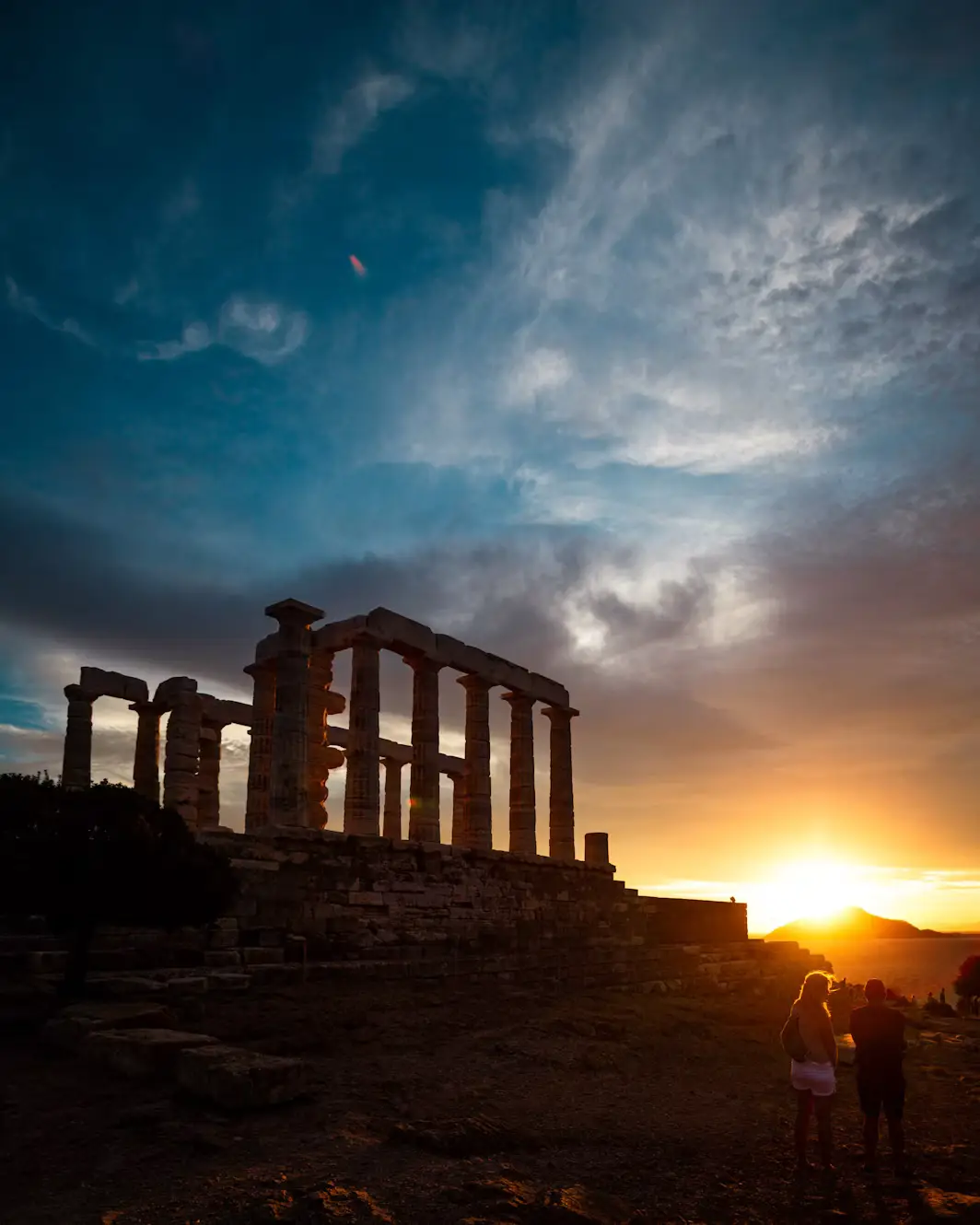 The ancient columns of the Temple of Poseidon at Cape Sounion silhouetted against a dramatic sunset sky.