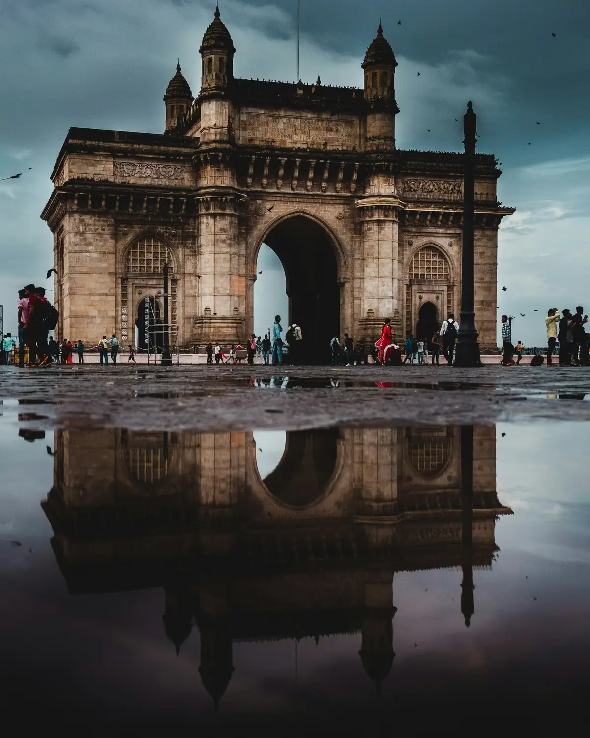 Gateway of India colonial basalt arch monument reflected in rain puddle with tourists, Mumbai, Maharashtra