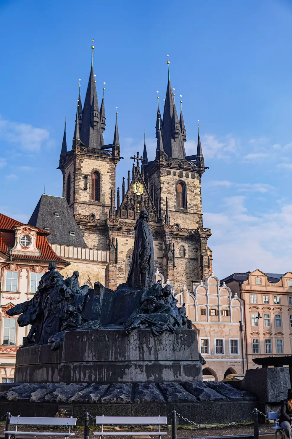 Jan Hus Memorial statue in Old Town Square with the twin Gothic spires of Týn Church behind it