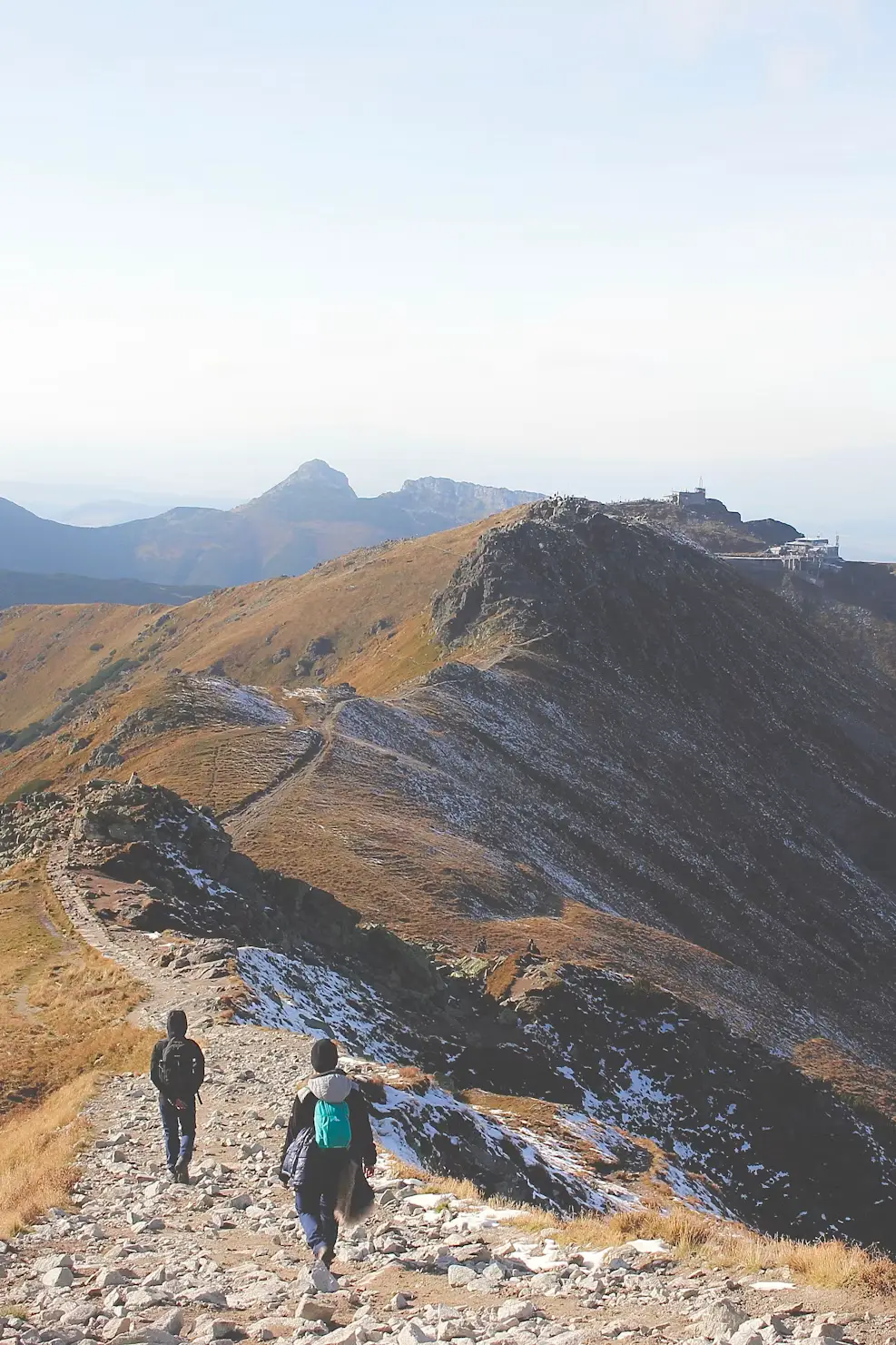 Hikers walking along a rocky mountain ridge with snow-dusted peaks in the distance, Poland.