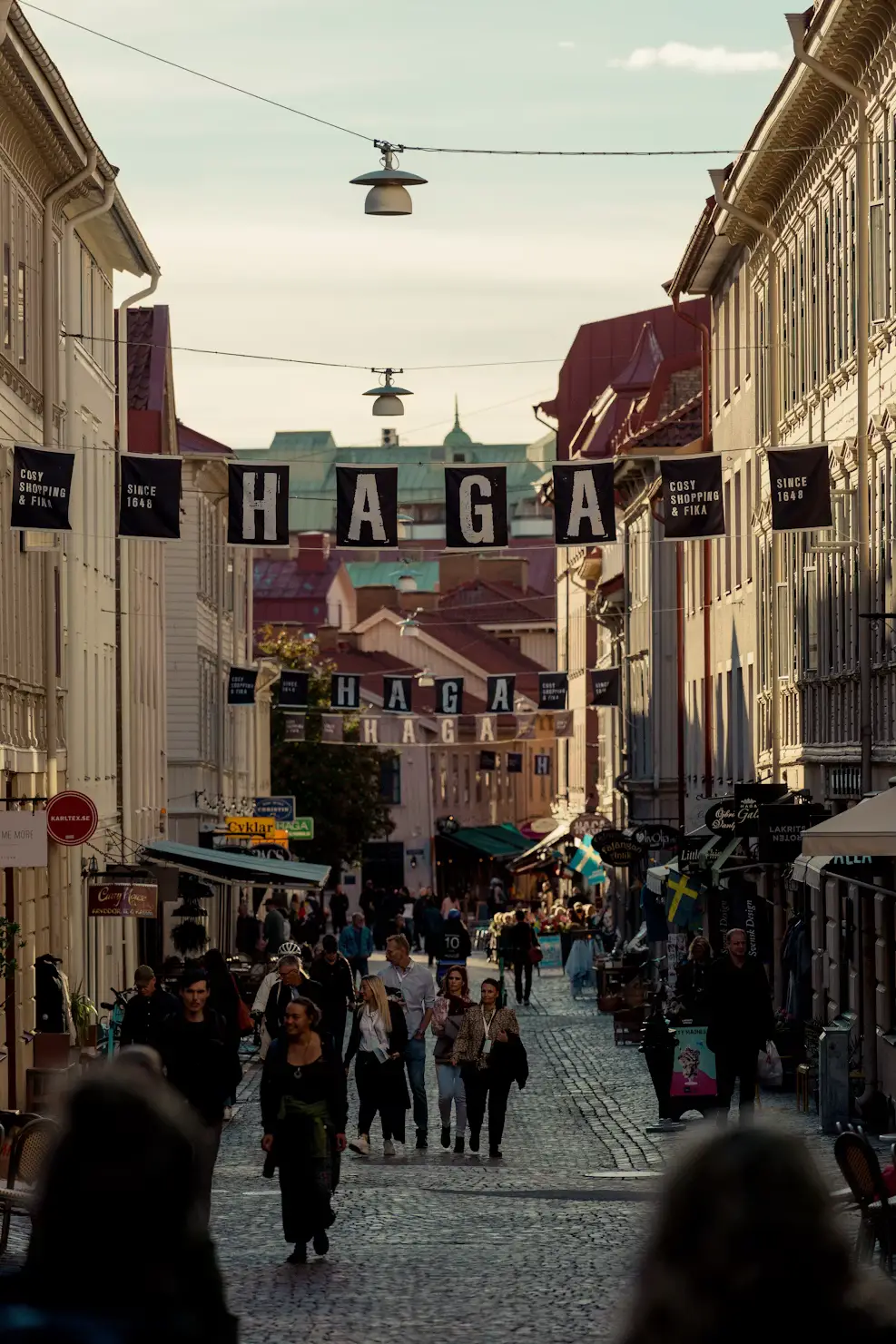 Crowd of pedestrians on a cobblestone street in the Haga district, with a sign reading "HAGA" strung between buildings.