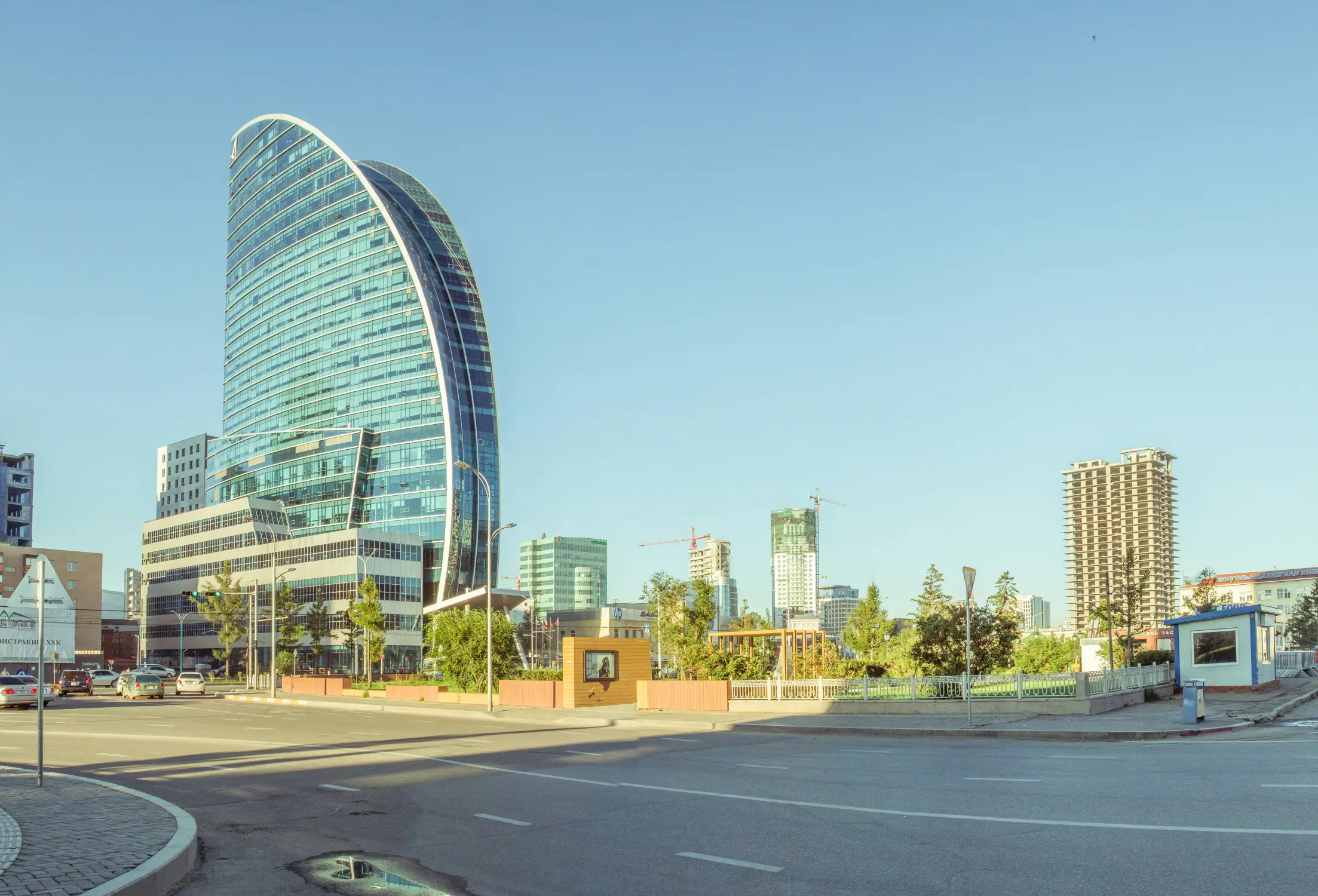 The Blue Sky Tower, a landmark curved glass skyscraper in downtown Ulaanbaatar, Mongolia, with the modern city skyline and construction cranes in the background