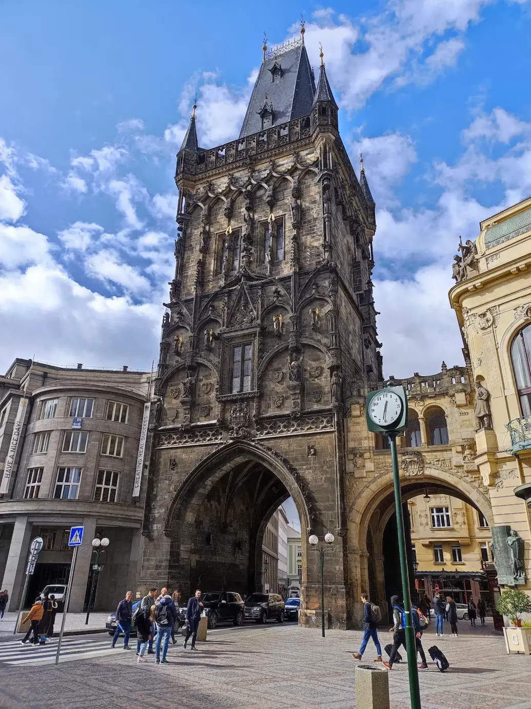 Powder Tower Gothic gate in Prague against a blue sky, with pedestrians passing below.