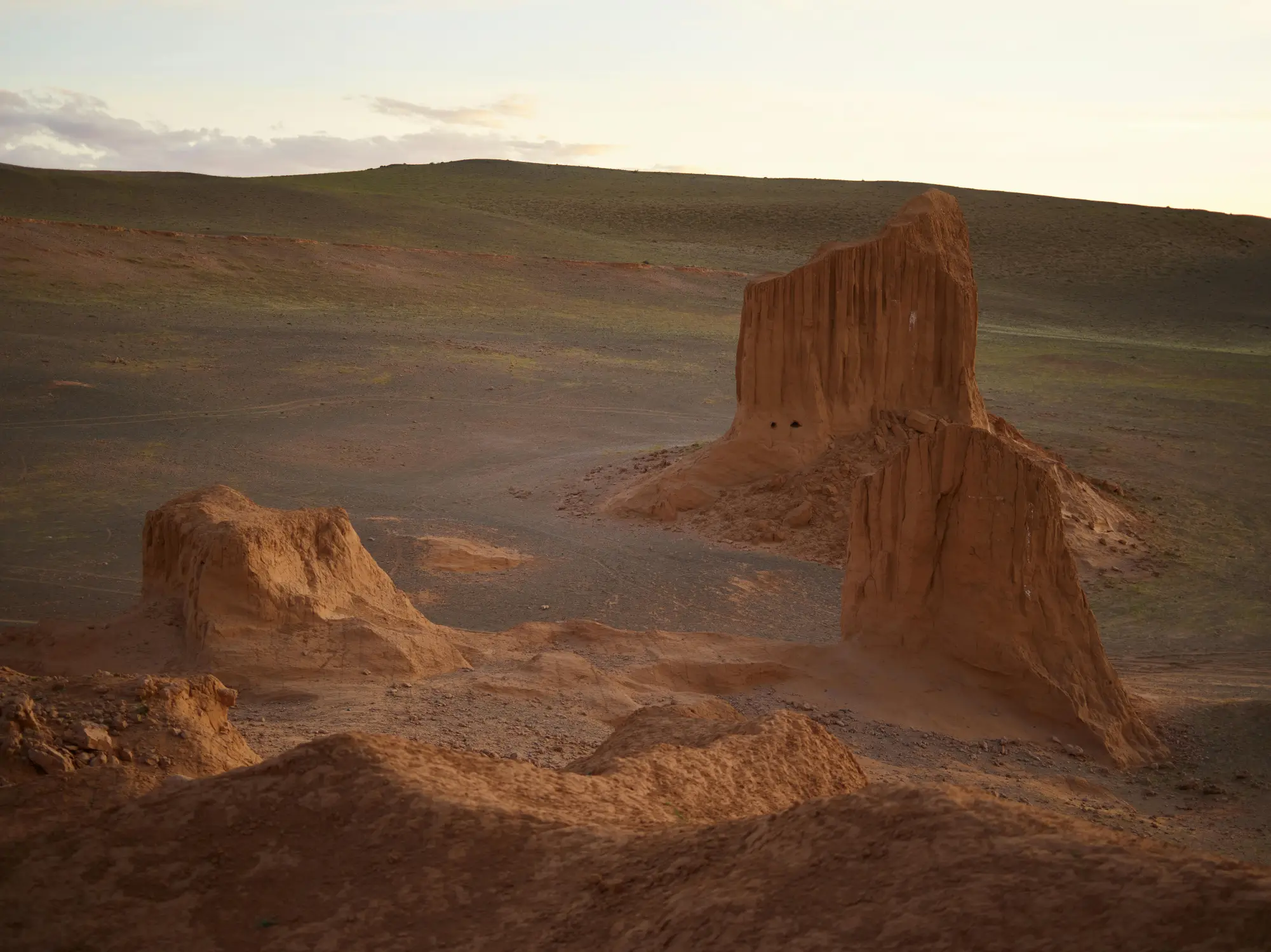 Dramatic red sandstone rock formations at golden hour in the Gobi Desert, Mongolia, with green steppe hills in the background
