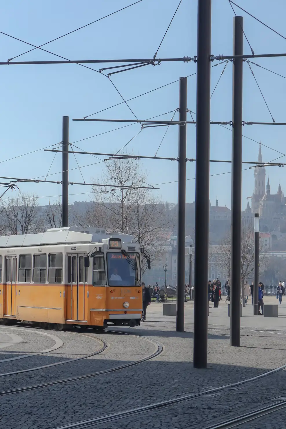 Yellow tram on curved tracks with overhead wires and church spires in the distance.