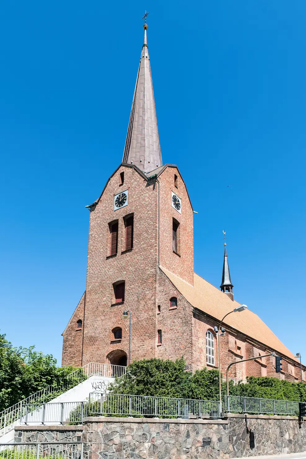 Red-brick church with a tall spire in Denmark under a clear blue sky
