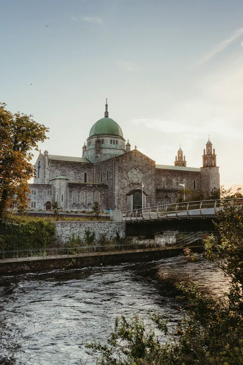 Historic cathedral with a green dome beside a flowing river at dusk, Galway, Ireland.