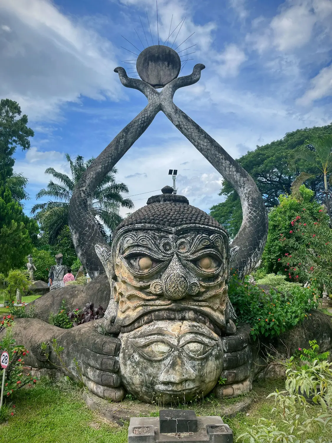 Large stone deity sculpture with raised arms among palm trees at Buddha Park near Vientiane, Laos.
