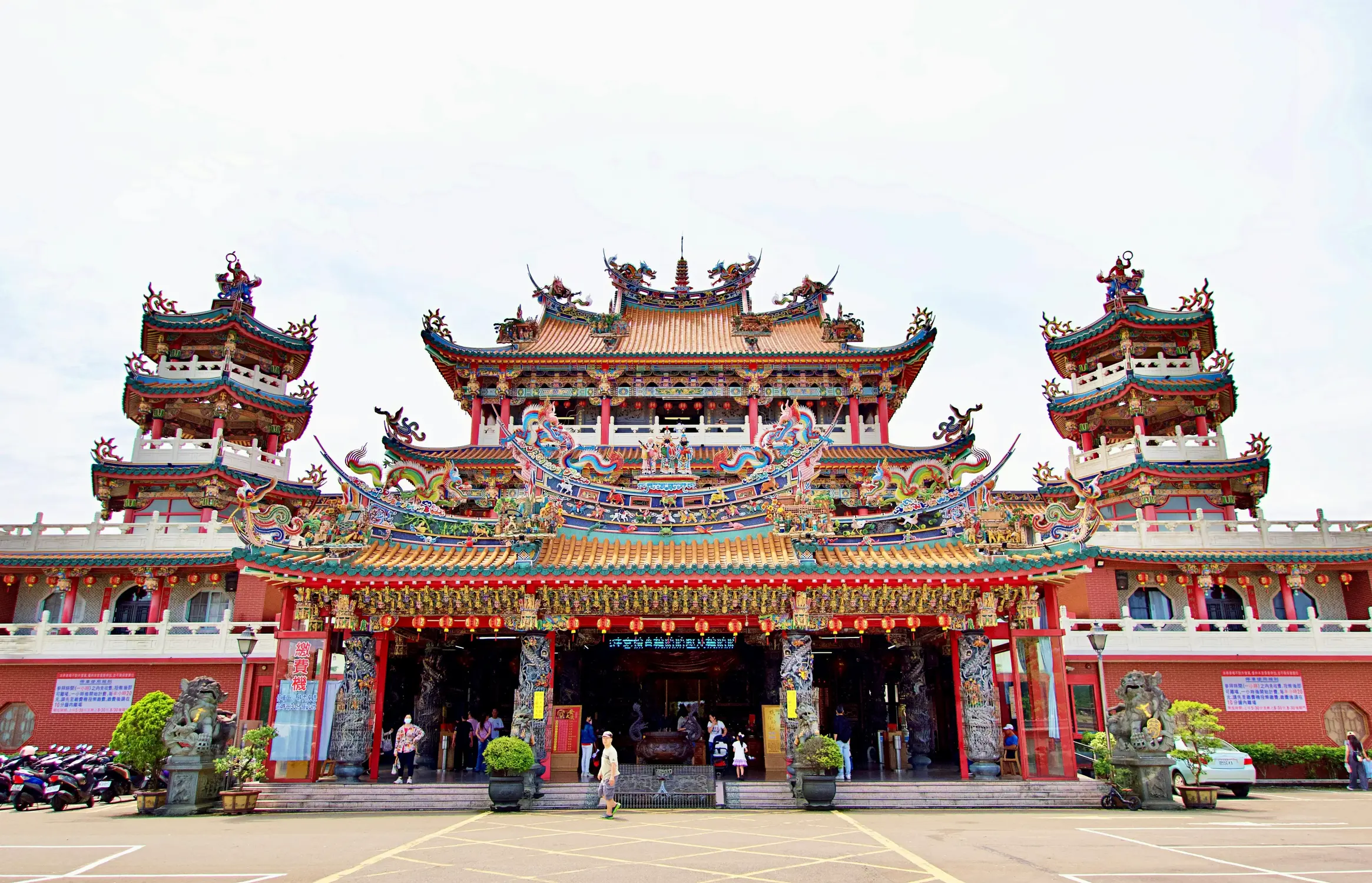 Ornate traditional Taiwanese temple with colourful dragon roof carvings, flanking pagoda towers, red columns, and stone guardian lions at the entranceOrnate traditional Taiwanese temple with colorful dragon roof carvings, flanking pagoda towers, red columns, and stone guardian lions at the entrance