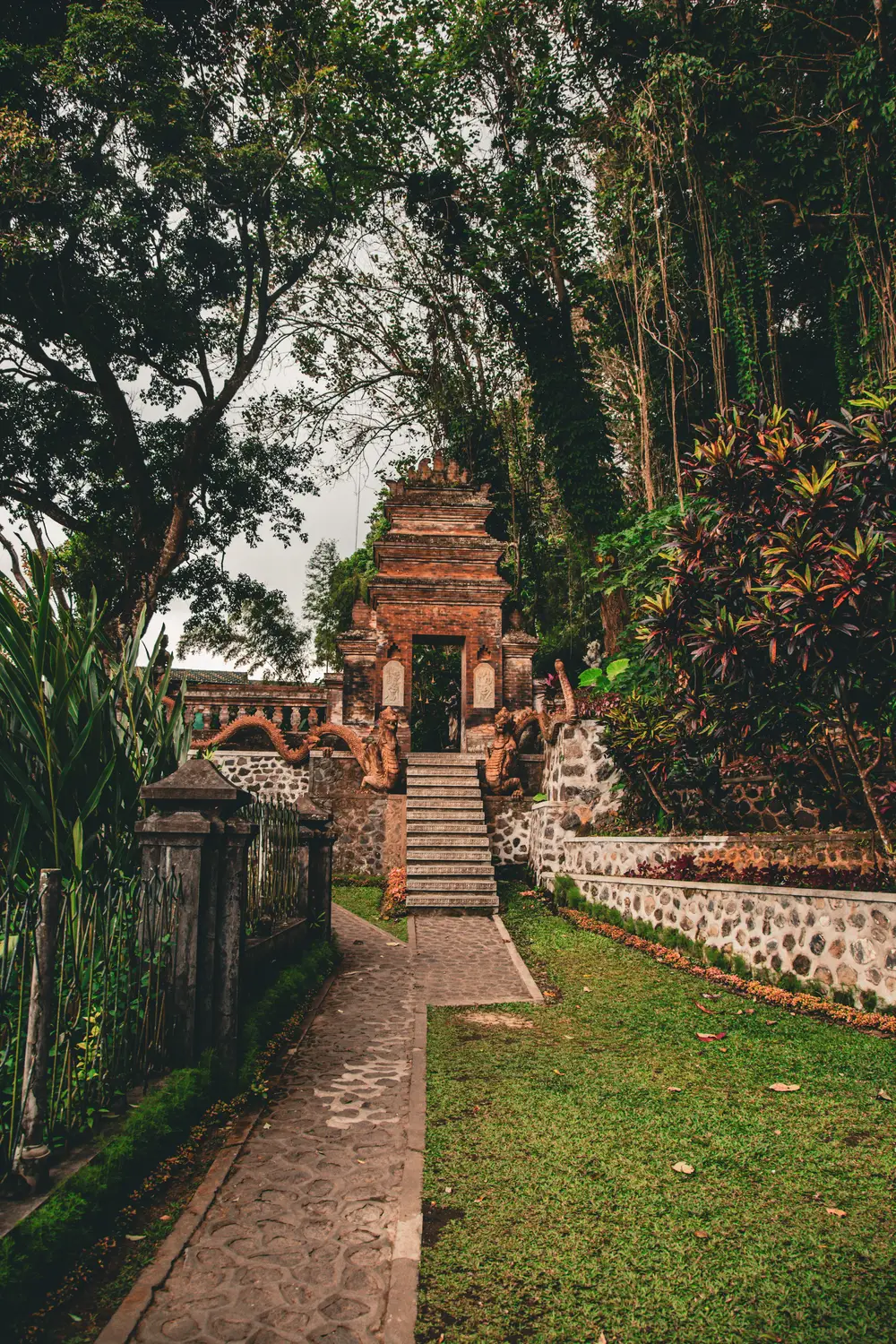 Stone pathway leading to an ancient Balinese temple surrounded by lush tropical trees and greenery in Bali, Indonesia.