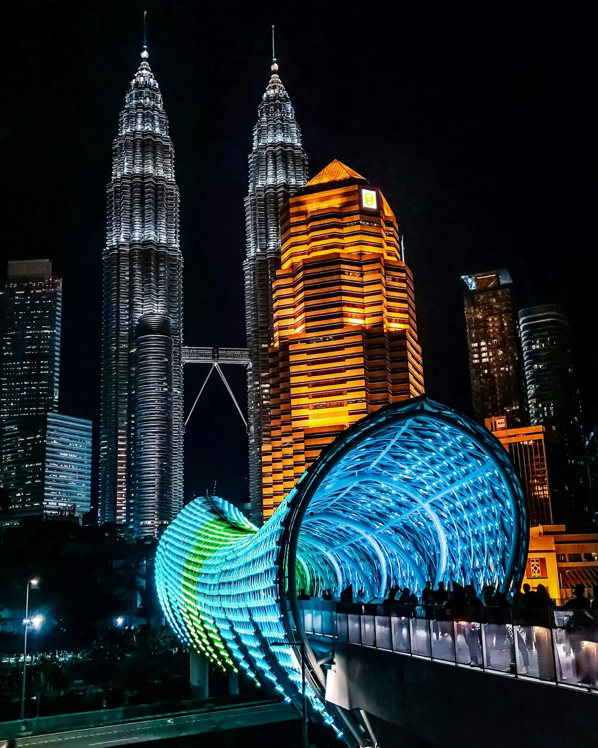 Petronas Twin Towers illuminated at night with glowing blue geometric sculpture in foreground at KLCC park Kuala Lumpur Malaysia