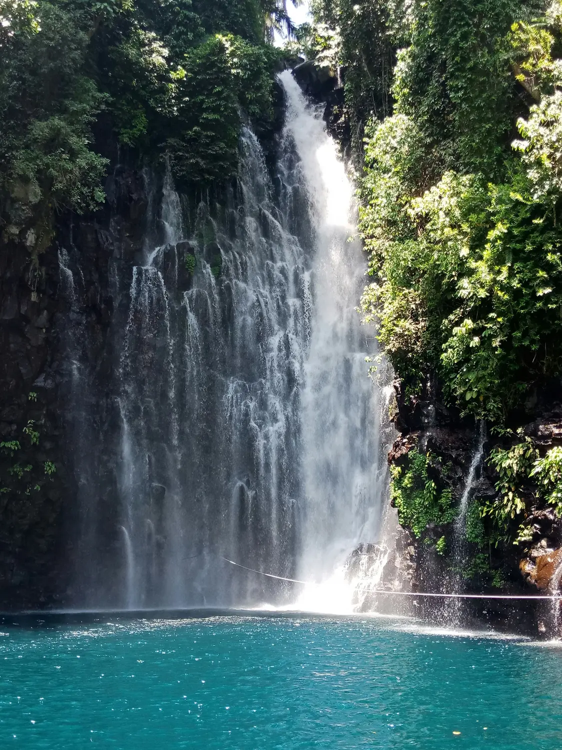 Tiered waterfall cascading into a turquoise pool surrounded by lush green forest in the Philippines.