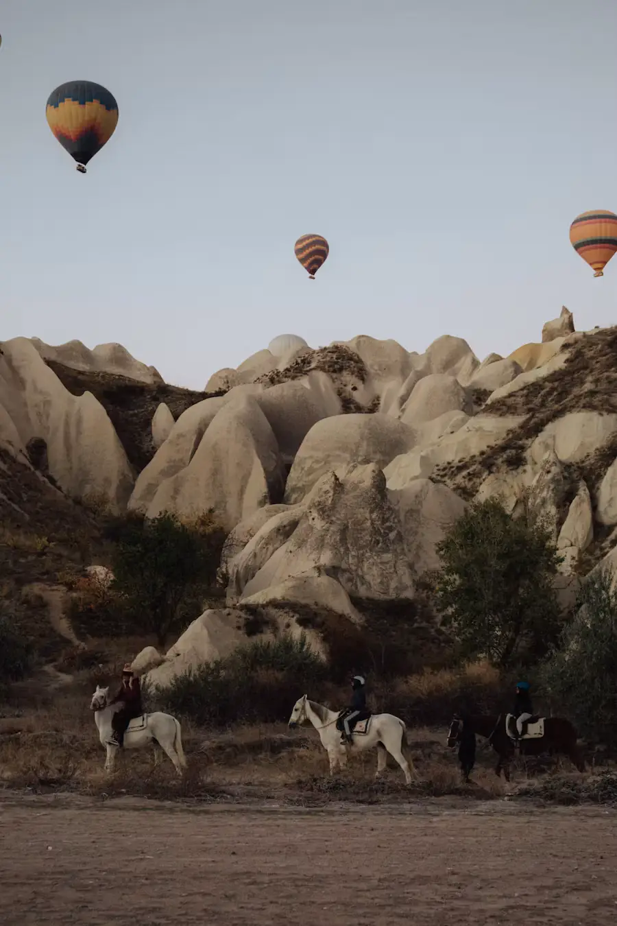 Hot air balloons rising above rocky, cone-shaped rock formations in Cappadocia, Turkey, in the early morning light.