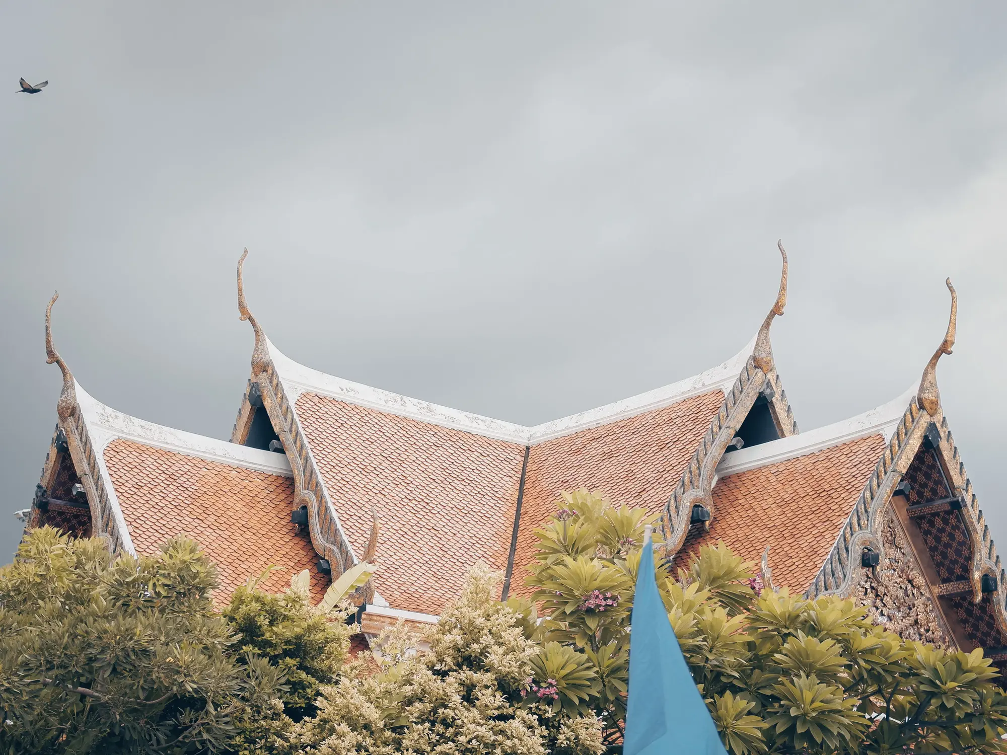Twin peaked temple roofs with gilded finials rising above green treetops under a cloudy sky.