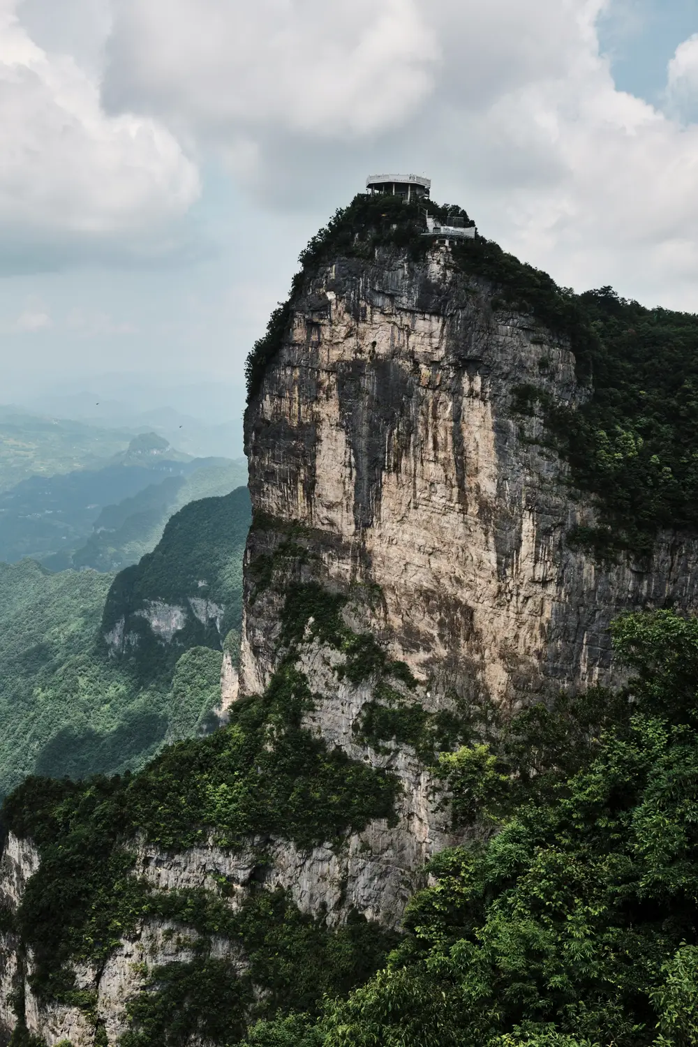 Dramatic karst limestone cliff peak with observation platform at summit surrounded by lush green mountains, Zhangjiajie China