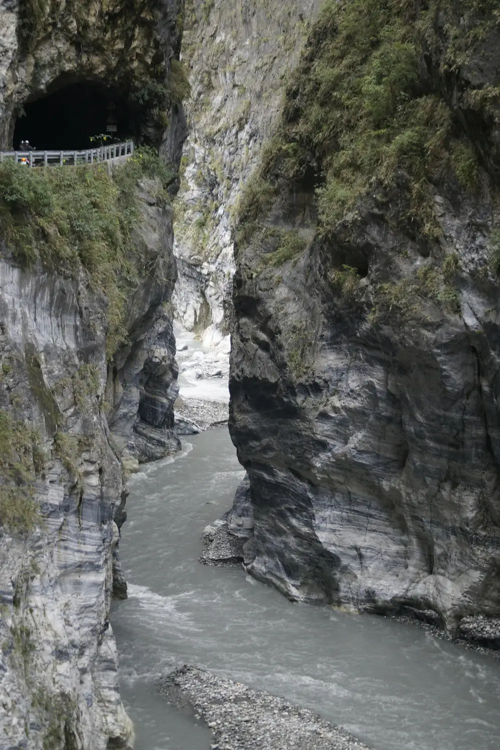 River carving through towering marble cliffs in Taroko Gorge, with a tunnel and roadside railing cut into the rock face
